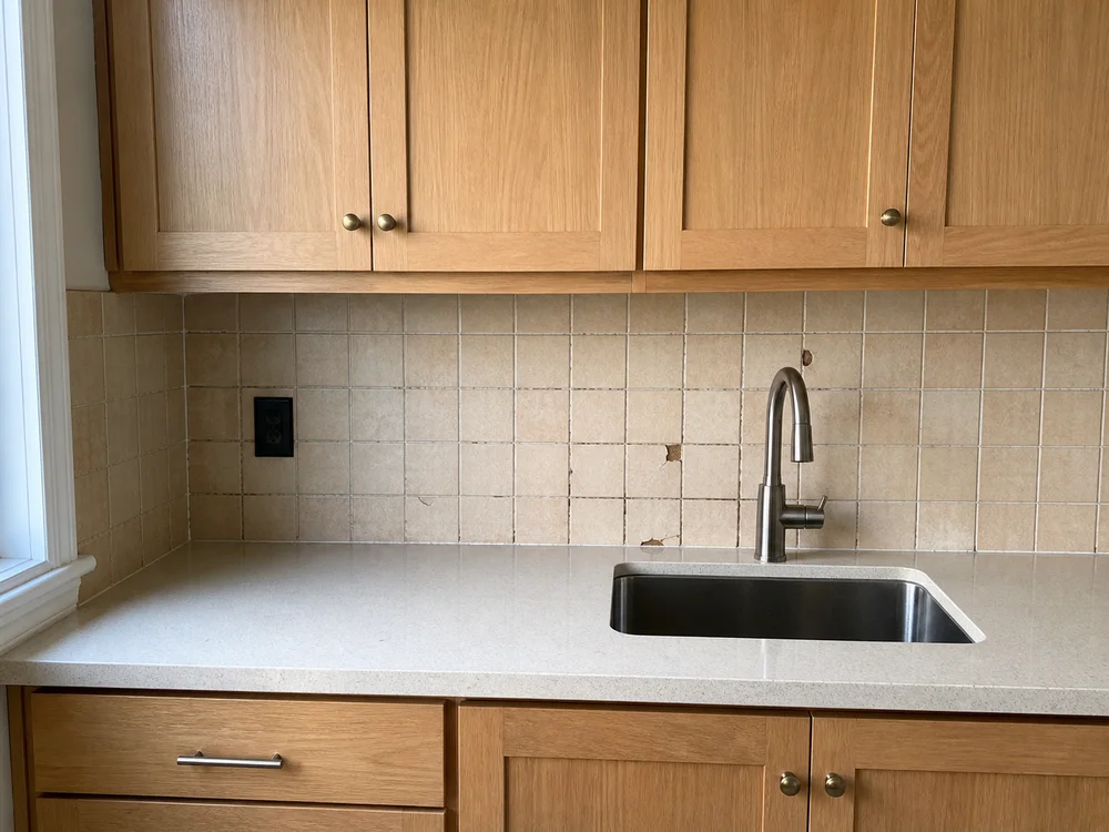 Kitchen before the example repair, with beige backsplash tiles and damaged grout